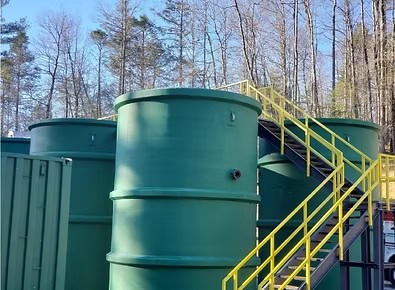 Large green wastewater treatment tanks with staircases, used in water recycling and environmental sustainability.